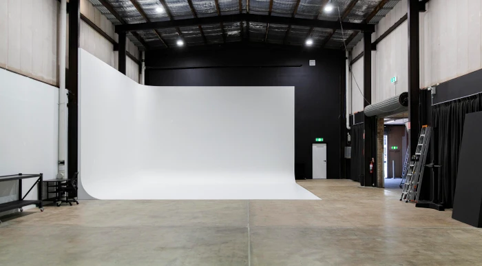 Wide angle view of a large photography studio featuring a white cyclorama wall and concrete floors