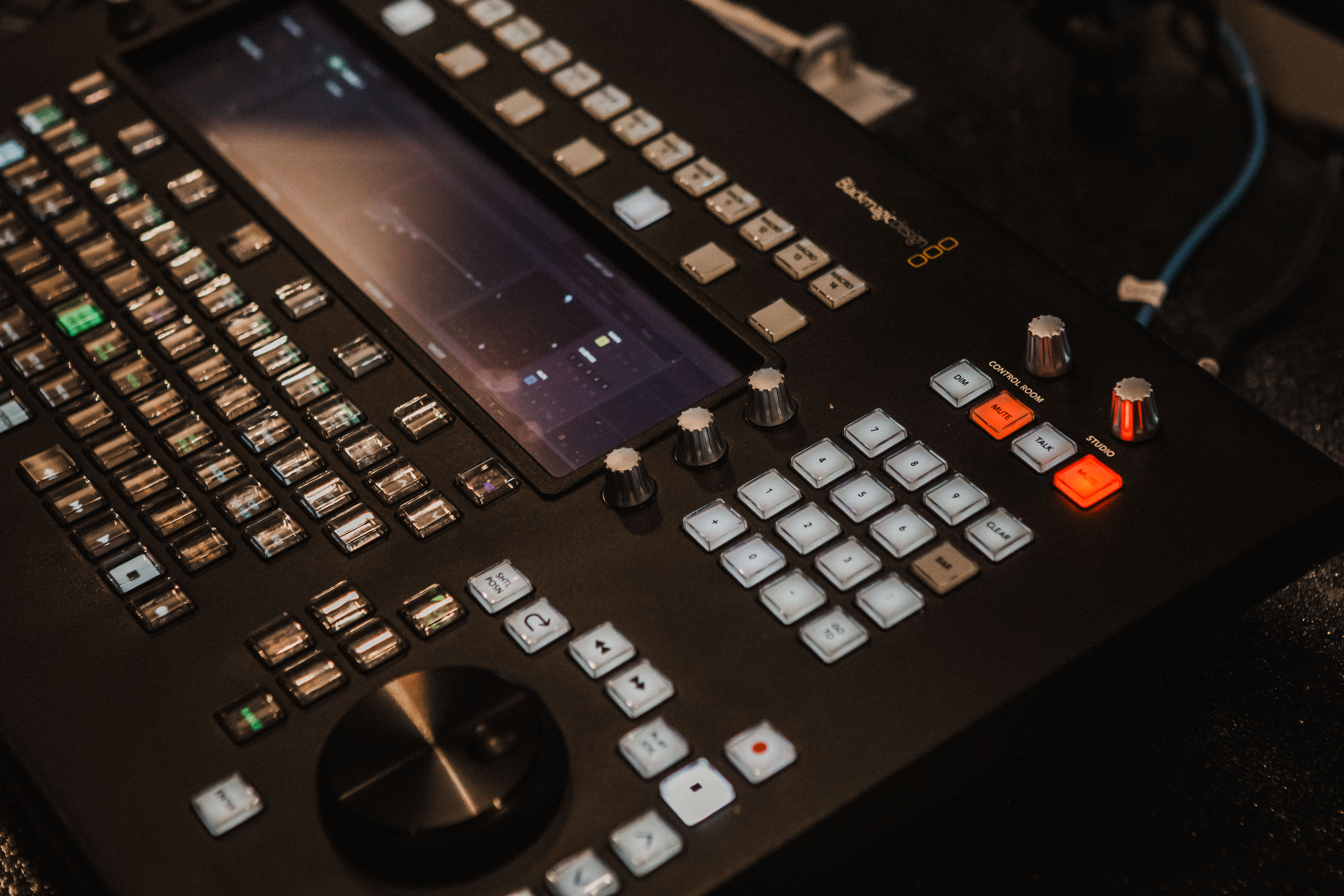 Close-up view of a professional Blackmagic video switcher with a variety of buttons, knobs, and a central display screen for broadcast control.