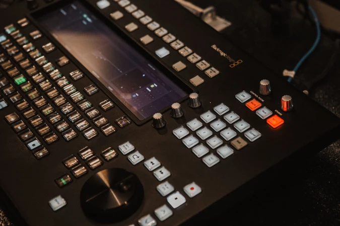 Close-up view of a professional Blackmagic video switcher with a variety of buttons, knobs, and a central display screen for broadcast control.