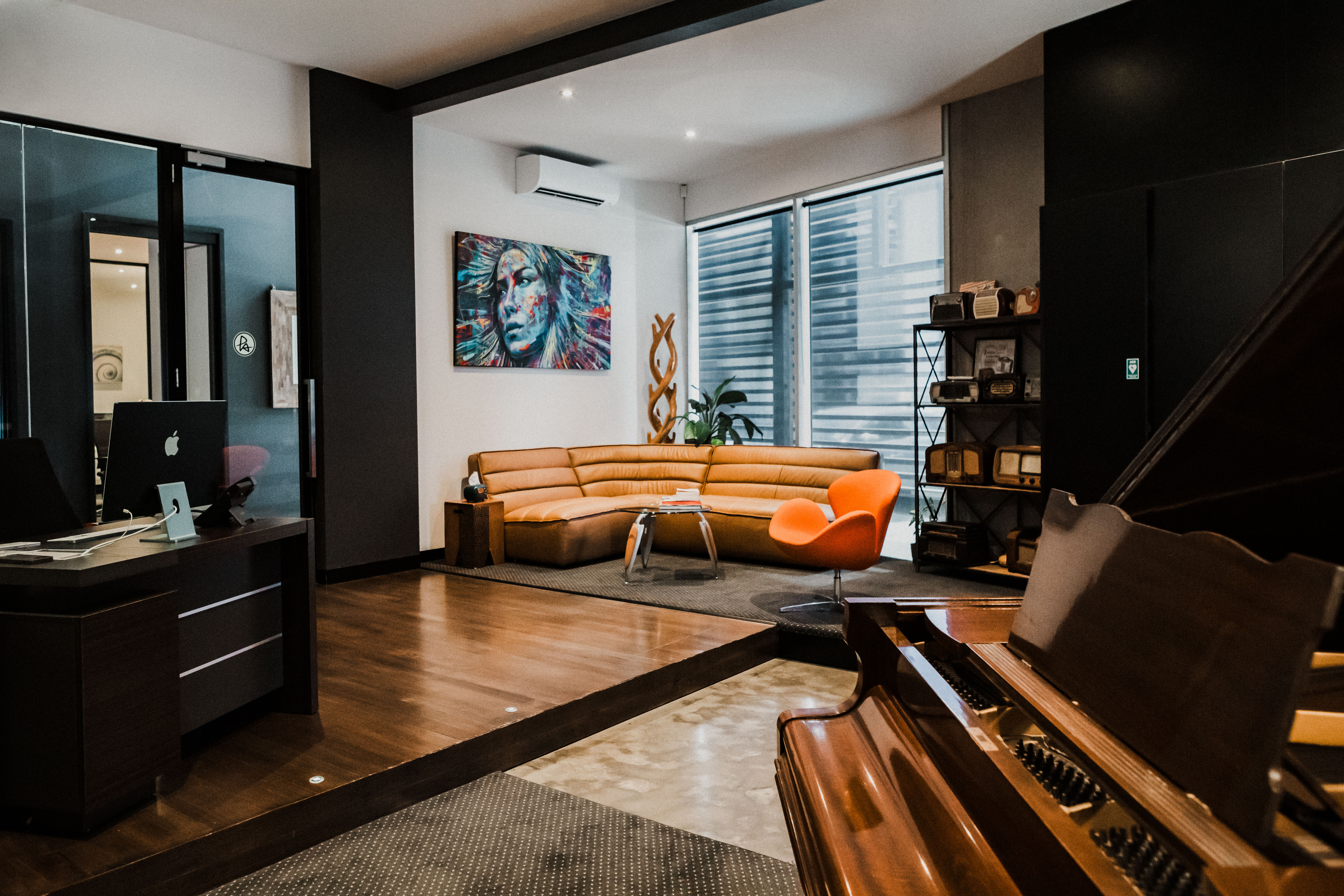 Contemporary music studio featuring a grand piano, modern furniture, artwork, and a vintage radio collection in a stylish indoor setting.