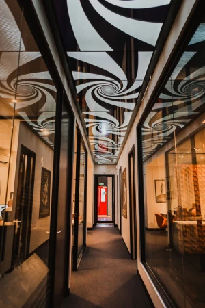 Interior shot of a long office hallway with a spiral pattern on the ceiling, doors to the offices along both sides and a red door in the distance.