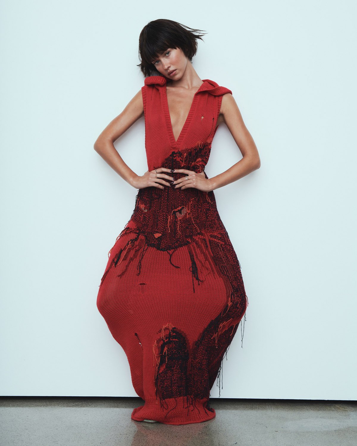 Elegant woman in a stylish red knit dress posing against a white wall with a modern and artistic flair, fashion forward.