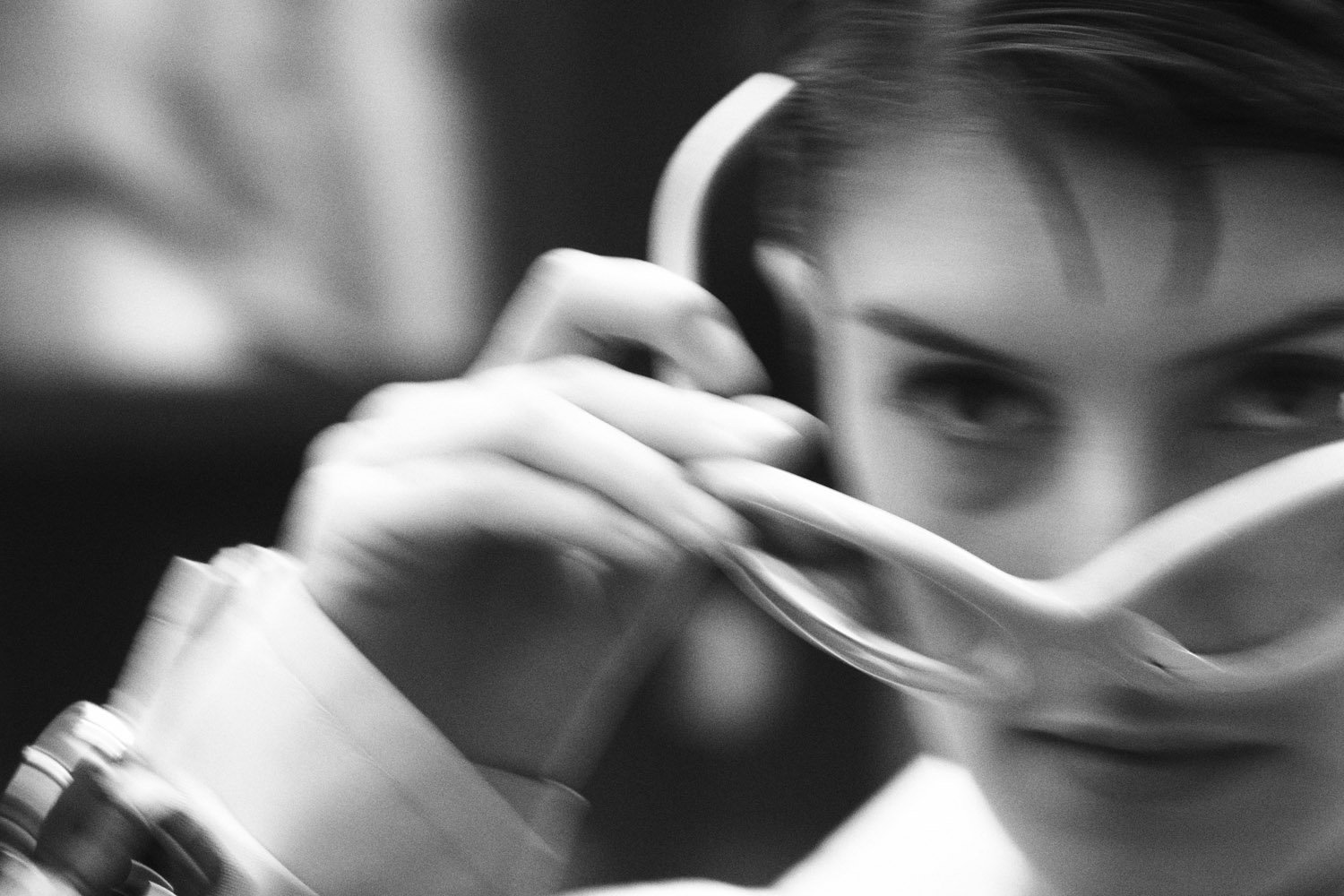 Close-up black and white portrait of a woman putting on white sunglasses. She looks directly at the camera with a neutral expression.