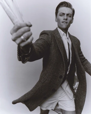 Man wearing a tweed blazer and white shorts holding up stalks styled by Patrick Zaczkiewicz against a neutral background