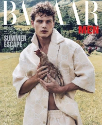 A male model holding a chicken outdoors, wearing a textured cream designer coat styled by Patrick Zaczkiewicz.