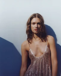 Woman wearing a shimmering sequin dress standing against a light wall with strong shadows.