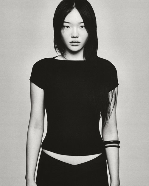 Portrait of an Asian woman in a dark top and bottoms, looking at the camera with a serious expression against a neutral backdrop.