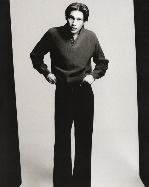 Monochrome portrait of a male model in a casual knit sweater and wide-leg pants, posing against a clean studio backdrop with soft lighting.