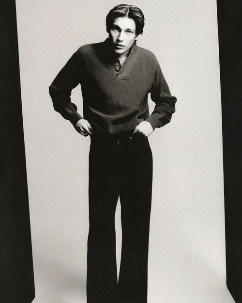 Monochrome portrait of a male model in a casual knit sweater and wide-leg pants, posing against a clean studio backdrop with soft lighting.