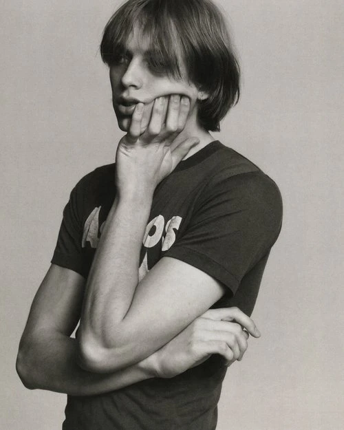 Monochrome portrait of a young adult with hand on face, wearing a t-shirt, posing in a neutral indoor studio setting.