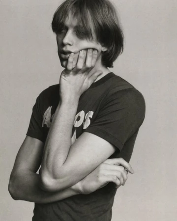 Monochrome portrait of a young adult with hand on face, wearing a t-shirt, posing in a neutral indoor studio setting.