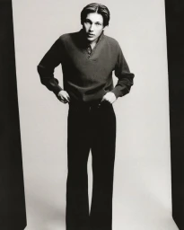 Young man in a dark polo sweater and trousers posing against a light backdrop in portrait orientation.