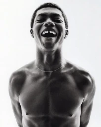 Portrait of a smiling young Black man with a thin silver necklace against a bright white seamless background.