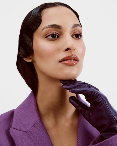 Headshot of a sophisticated woman in a violet blazer and dark gloves against a bright backdrop showcasing beauty and fashion style.