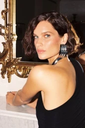 Woman in black top with silver earrings looking over shoulder near gold framed mirror
