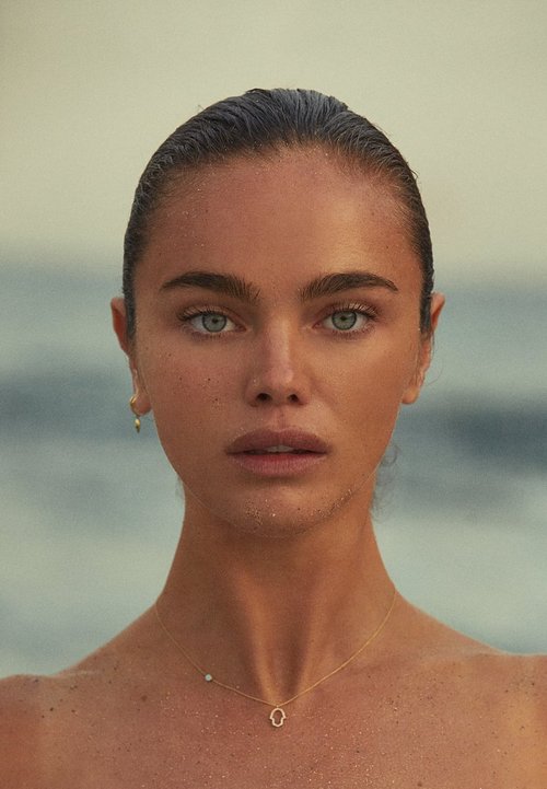 Close-up of a young woman with wet hair and a necklace against a light background. Beauty portrait focusing on her face and jewelry.