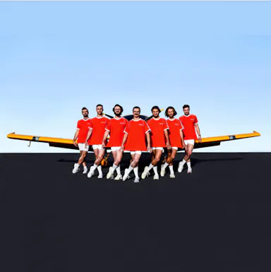 Seven men in matching outfits pose in front of a yellow airplane outdoors, wearing red shirts, white shorts, and sneakers on a tarmac.