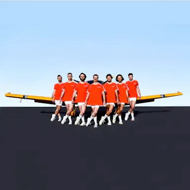 Seven men in matching orange t-shirts and white shorts posing in front of a yellow airplane against a blue sky