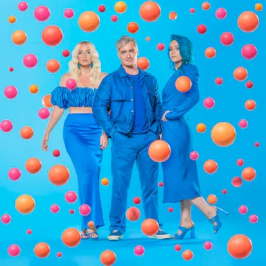 Three people in monochromatic blue outfits posing amidst floating orange and pink spheres against a bright blue background