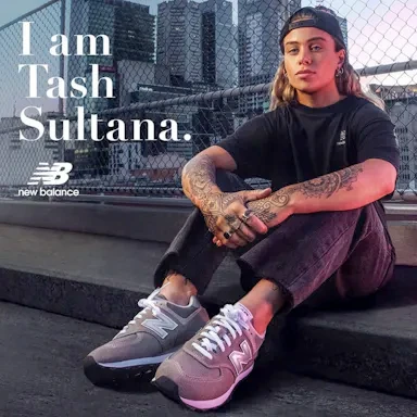 Tash Sultana sitting on a rooftop wearing a black t-shirt and grey sneakers with cityscape background