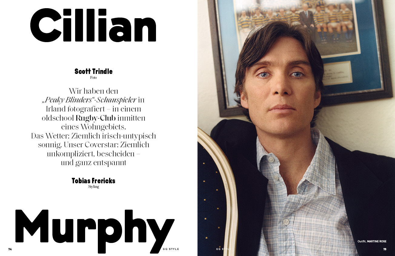 Portrait of actor Cillian Murphy in light grey patterned button-down shirt and dark jacket in a room with a framed photo on the wall.