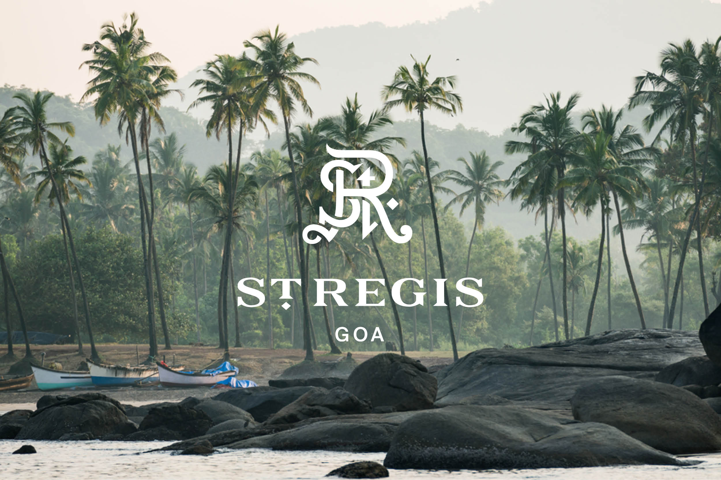 Scenic view of palm trees, boats on the shore, and large rocks under the St. Regis Goa logo, creating a serene coastal ambiance.