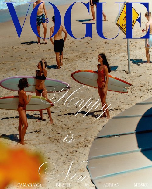 Magazine cover featuring a group of people on a sandy beach with surfboards, under the masthead 'Vogue,' and text 'Happy is Now'.