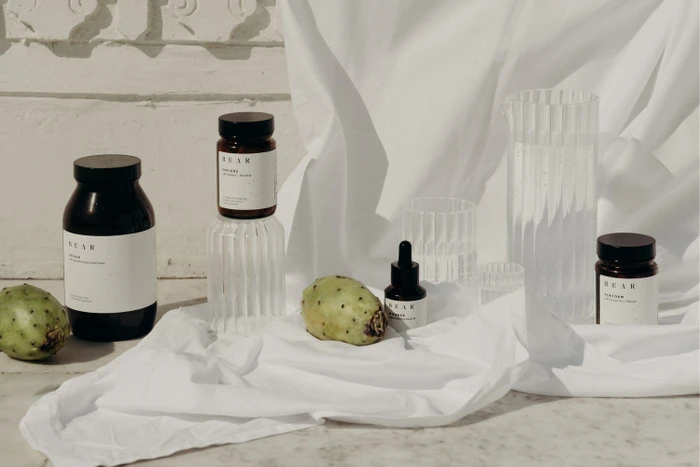 Product arrangement of amber glass supplement jars and dropper bottles draped in white fabric with prickly pears