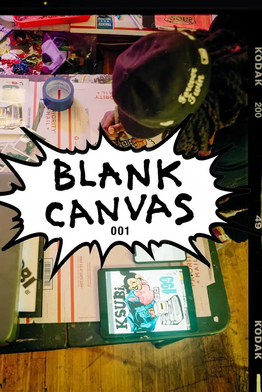 Overhead shot of a person drawing on a blank canvas, sitting at a table with art supplies, a tablet, and a graphic design.