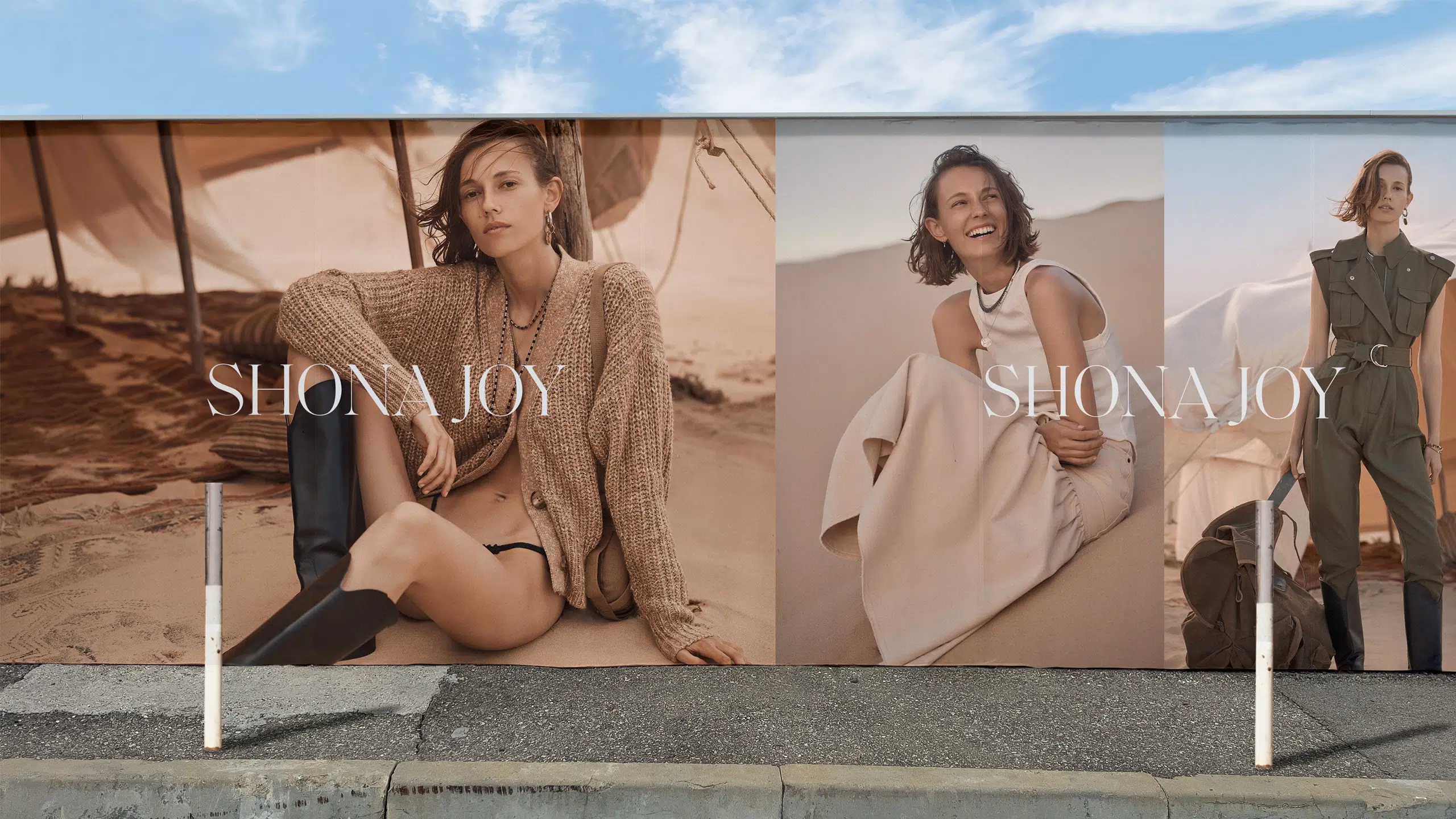 Fashion billboard featuring a young adult woman in casual clothing, set against a desert backdrop, promoting the SHONA JOY brand.