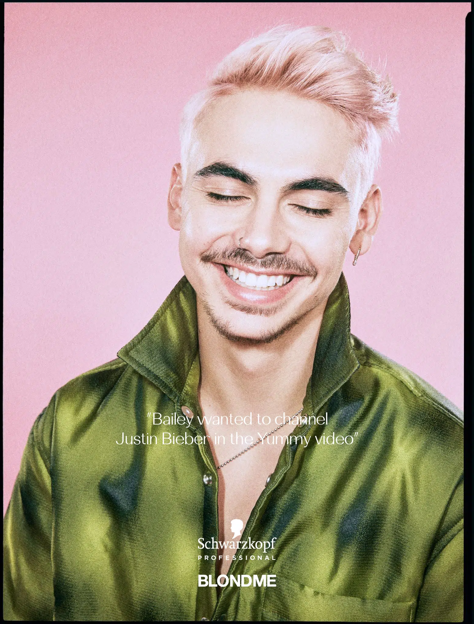 Close-up of a smiling adult male with pink-tinted hair in a green shirt against a pink backdrop, advertising hair products.
