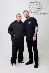 Two men standing together against a seamless white background with handwritten text above them.