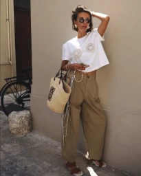 Woman in white t-shirt and khaki trousers leaning against a beige wall holding a straw tote bag in Sydney