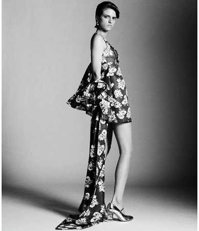 Monochrome fashion portrait of a woman in a floral dress and silver shoes in a studio with a neutral gray background.