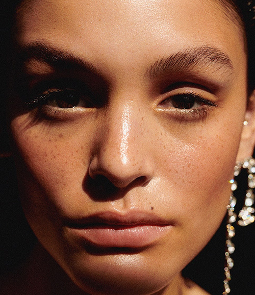 Close-up portrait of a woman with freckles, wearing dangling rhinestone earrings in a studio setting, bathed in a warm glow.