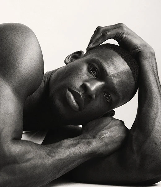 Black and white portrait of a muscular African-American man reclining, resting a hand on his head against a clean, bright background.