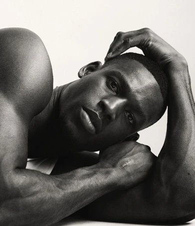 Black and white portrait of a muscular African-American man reclining, resting a hand on his head against a clean, bright background.