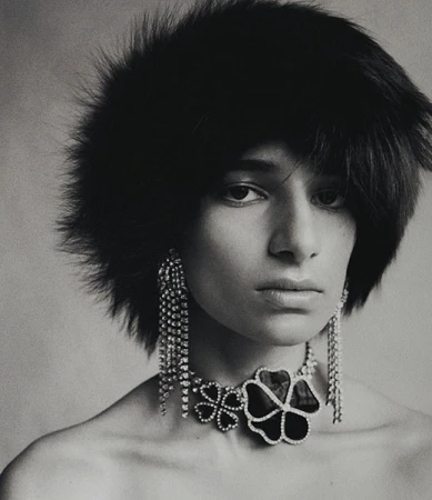 Close-up portrait of a model wearing a dark fuzzy hat, crystal earrings, and a floral statement necklace by Paul Scala