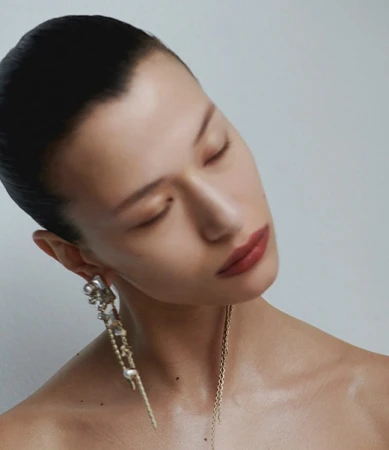 Close-up portrait of a woman with her eyes closed, wearing ornate pendant earrings against a plain light background by Paul Scala