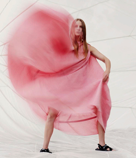 Fashion shot of a woman wearing a pink dress and black sandals against a white backdrop with blurred motion effect.