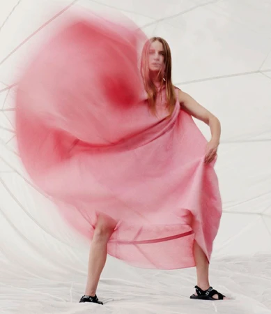 Model in a flowing pink dress captured with motion blur against a white geometric tent backdrop.