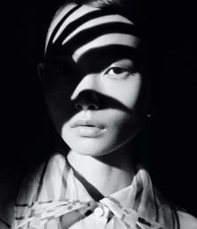 Close-up black and white portrait of a model with dramatic leaf shadows cast across her face.