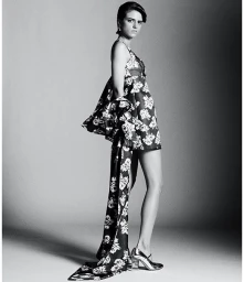 Model in a patterned floral dress with a long draped sash posing against a seamless studio background