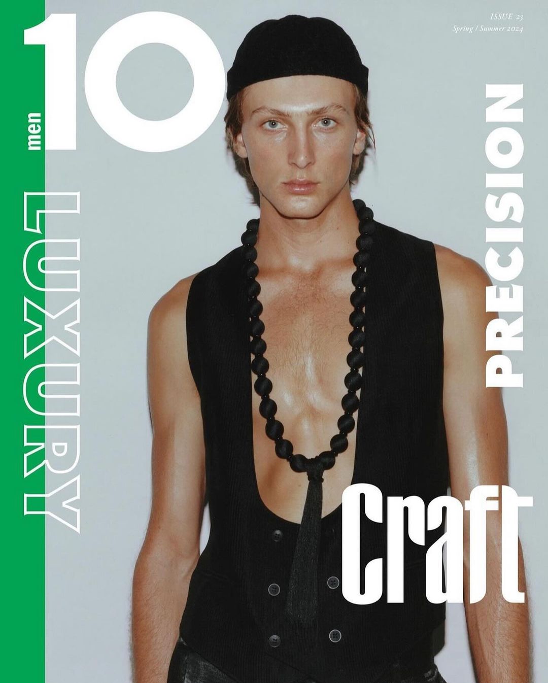 Fashion magazine cover featuring a male model wearing a black beanie, vest, and beaded necklace against a white backdrop.