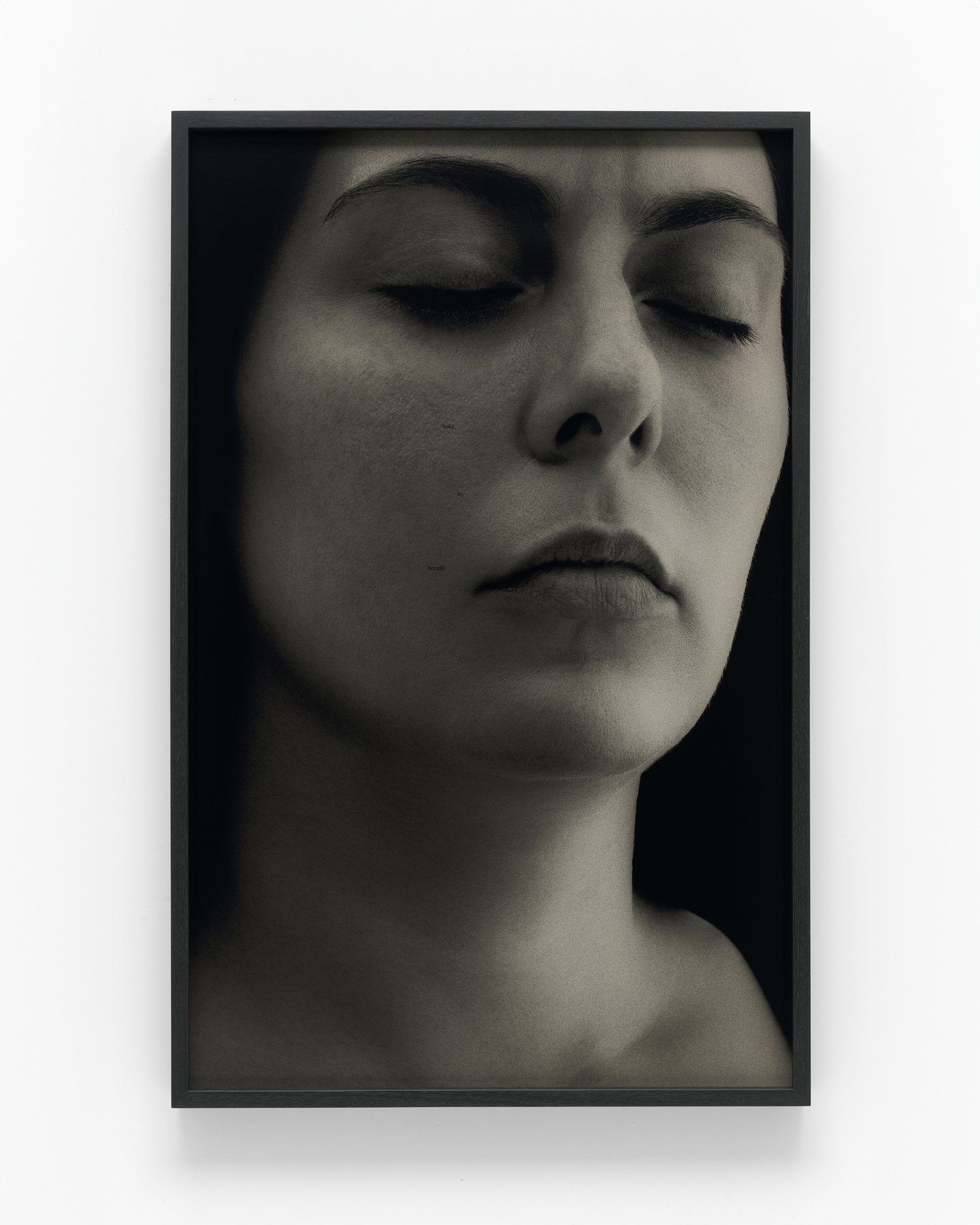 Monochrome photograph of a woman with eyes closed in a black frame against a white wall, evoking a sense of serenity.