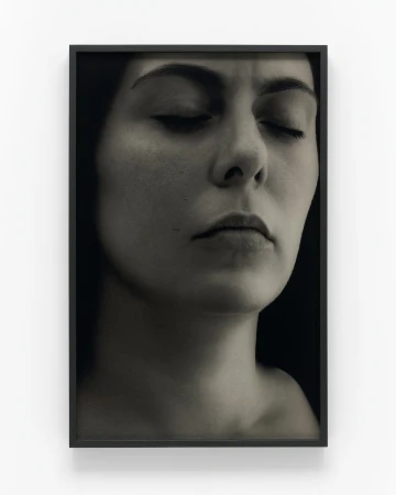 Monochrome photograph of a woman with eyes closed in a black frame against a white wall, evoking a sense of serenity.