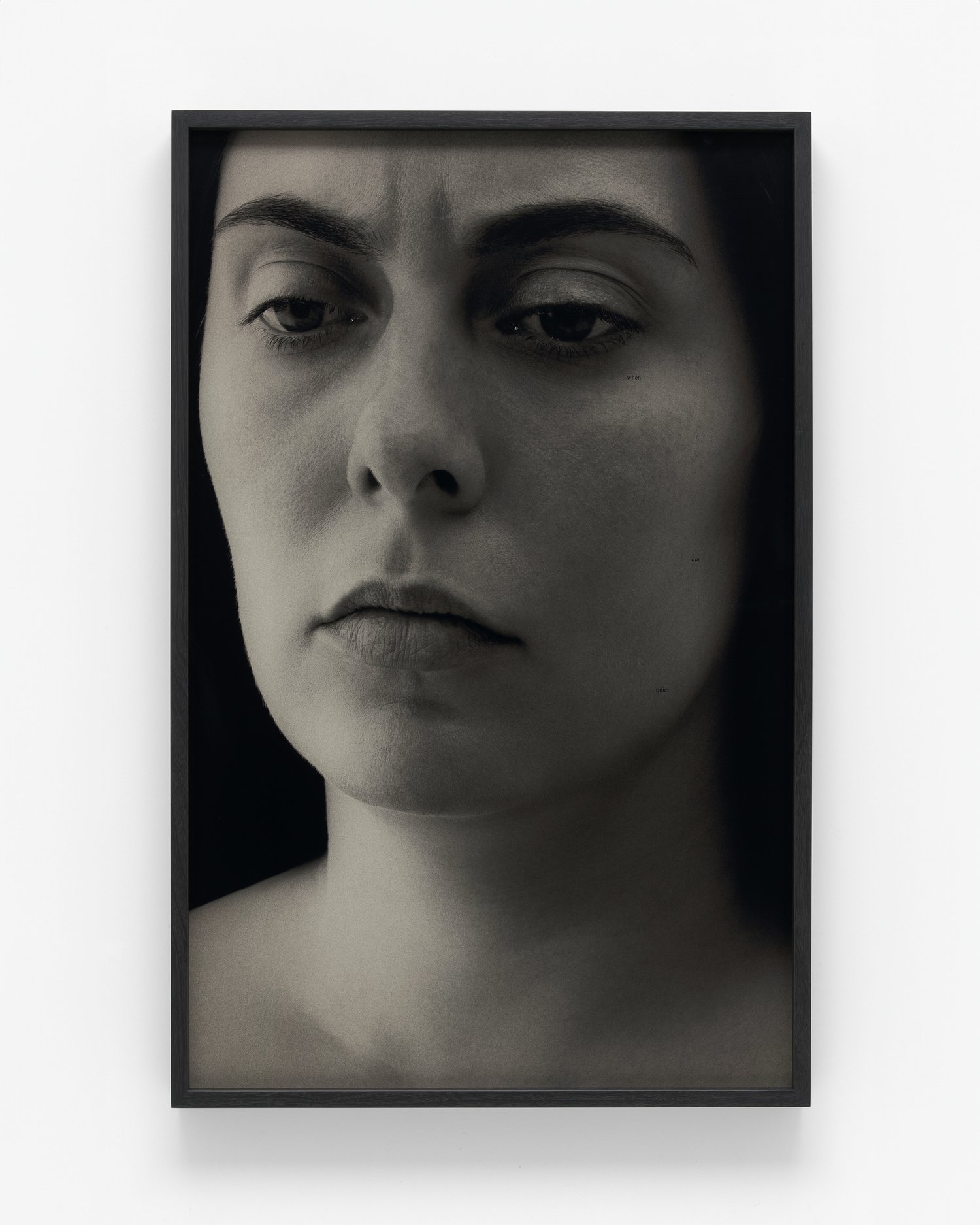 Monochrome portrait of a contemplative adult woman, gazing downward with neutral expression, framed against a stark black background.