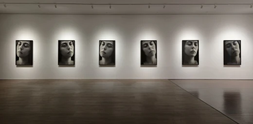 Six framed black and white portrait photographs hung in a row along a white gallery wall above a polished wooden floor.