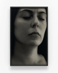 Monochrome portrait of a woman with closed eyes in a black frame against a white wall