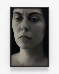 Framed monochrome portrait photograph of a woman with a serious expression against a plain white wall